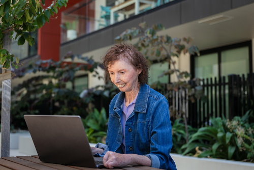 An image of Maria using her laptop in her apartment courtyard.