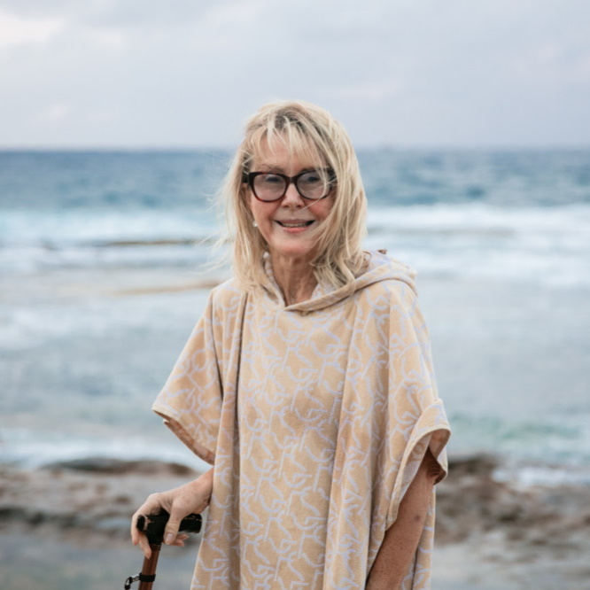 A woman standing in front of an ocean rock pool. She is holding an assistive walking cane.