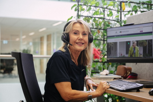 A woman sitting in front of a desktop computer. She is wearing a call headset and smiling.