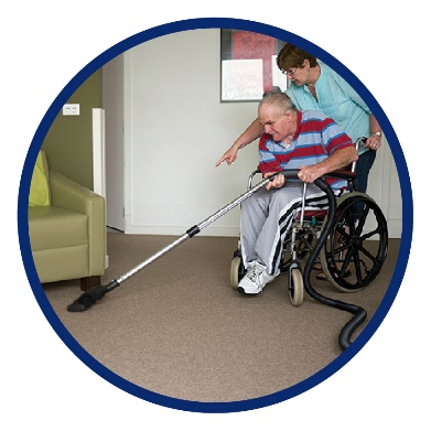 A woman helping a man in a wheelchair vacuum his house