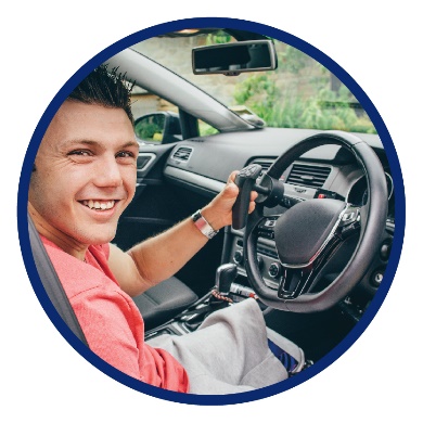 A man sitting in the driver's seat of a car smiling. There is an extra control on the steering wheel that he's holding