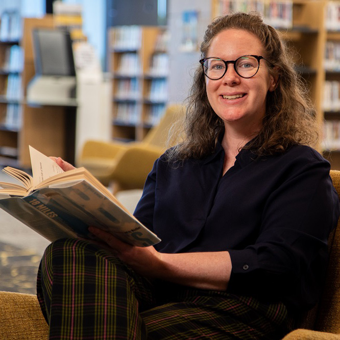 An image of Fiona smiling and holding a book in a library.
