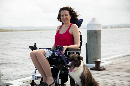 An image of Grace in her wheelchair by the wharf with her dog