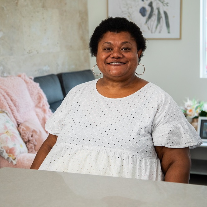 An image of Lowami sitting in her home smiling