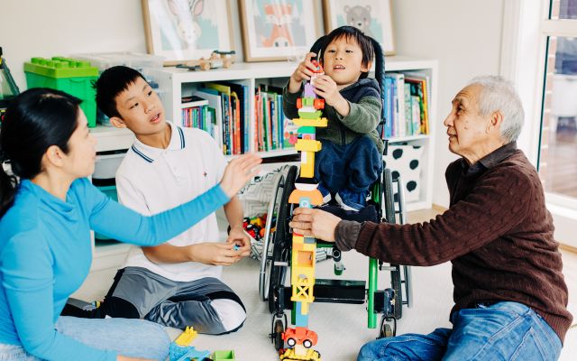 Image of a child playing with a tower of building blocks surrounded by 3 adults